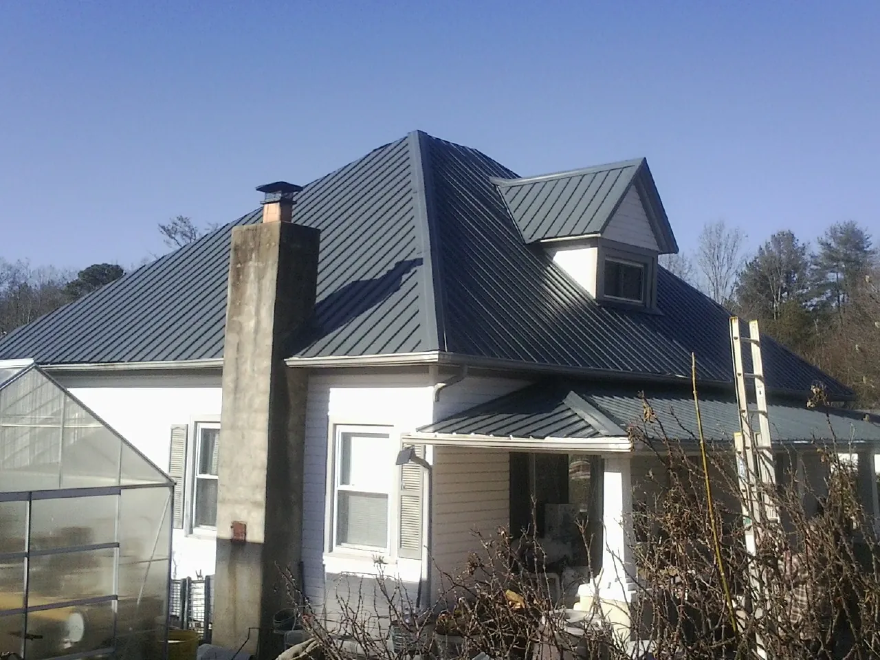 Dark blue standing seam metal roof on a white farmhouse with dormer — Slate & Tile Roof Repair by Roofing Brothers in Hartfield