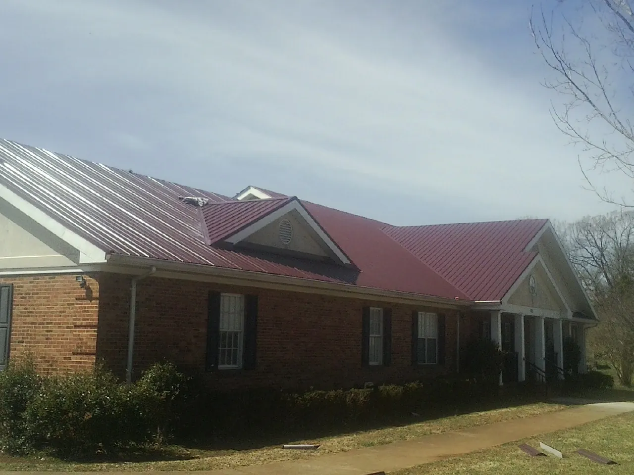 Red metal roof with gabled entries on a long brick building, from a Hail Damage Roof Repair job in Hartfield