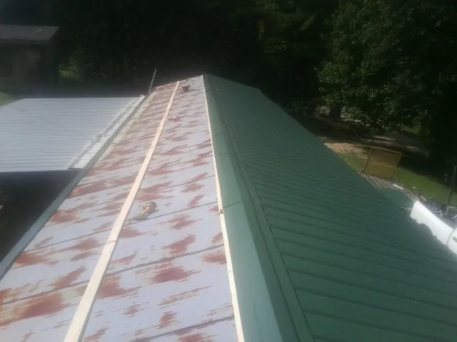 Old rusted panels beside newly installed green metal roofing — Wind Damage Roof Repair by Roofing Brothers in Hartfield