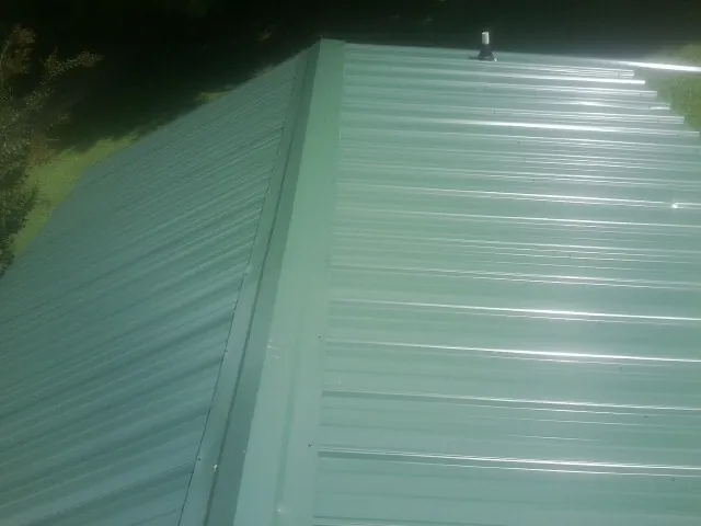New green metal panels meeting at the ridge of a roof — Flat Roof Repair work by our crew in Hartfield