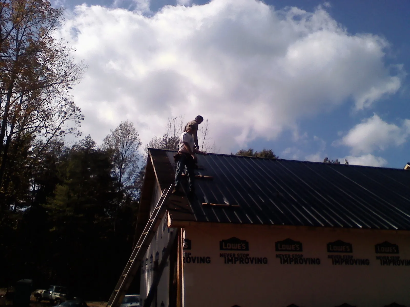 Roofer fastening dark metal panels high against a cloudy sky, from a Roof Inspection job in Hartfield