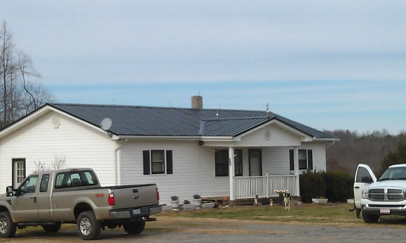 Finished dark metal roof on a white ranch home with work trucks parked in Hartfield
