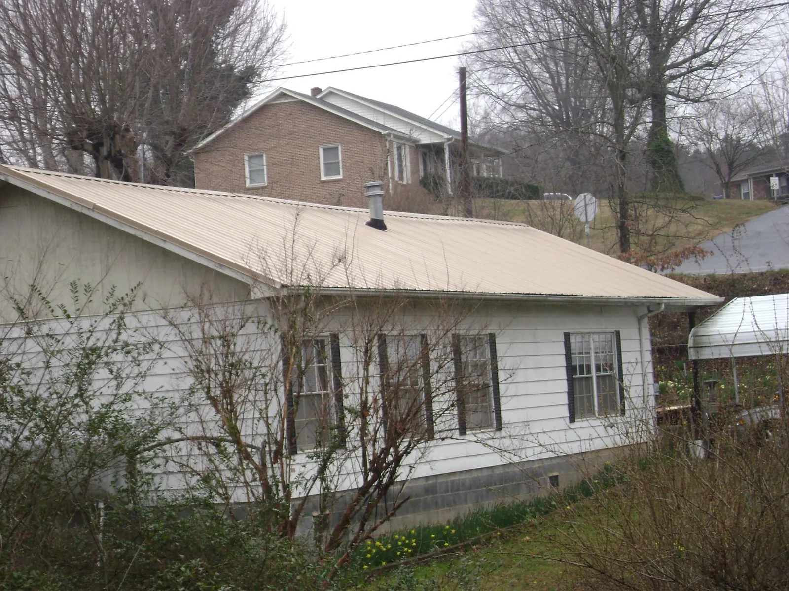 Tan metal roof on a white sided house set into a hillside — Commercial Roofing by Roofing Brothers in Hartfield